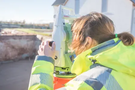 Kobieta w żółtej kurtce. Spogląda przez tachimetr.